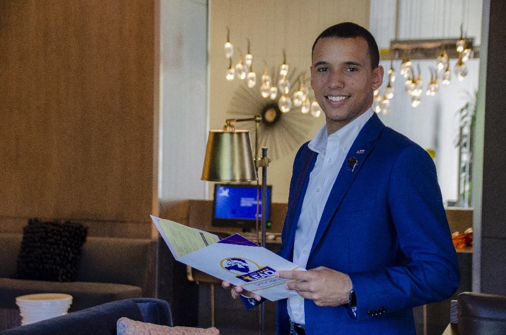 a young male marketing professional holding a folder and smiling at camera